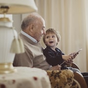 Un vieille homme tient assis sur ses cuisses un enfant qui le regarde en souriant.  