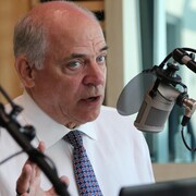 Un homme parle en gesticulant devant un micro dans un studio de radio. 