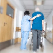 Une préposée aide un patient à circuler dans un corridor d'une résidence pour personnes âgées.