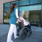 Une femme pousse le fauteuil roulant d'un homme à l'entrée d'un édifice.