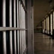Le corridor d'une prison avec à gauche un gros plan sur les barreaux d'une cellule.