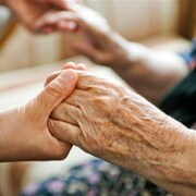 Une proche aidante tient la main d'une personne âgée.