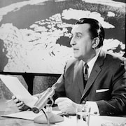 Jean-Paul Nolet lit le Téléjournal de Radio-Canada en regardant devant lui et en tenant une feuille de papier.