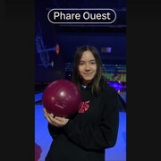 La jeune fille tient une boule de bowling dans les mains et elle sourit.