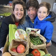 Une femme, un homme et leur fils posent devant un carton de fruits et légumes et de denrées non périssables.