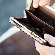 Des mains de personne âgée tiennent un petit porte-monnaie vide. 