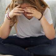 Une jeune fille est assise sur un sofa et elle se tient la tête dans les mains.