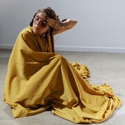 Une artiste drapée de jaune se frotte de la terre sur le visage. 