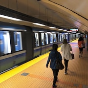 Des gens marchent sur le quai du métro, alors qu'un train passe. 