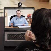 Une femme assise à un bureau s'adresse à un médecin par téléconférence sur un ordinateur.