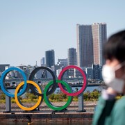 Il marche devant les anneaux olympiques à Tokyo.