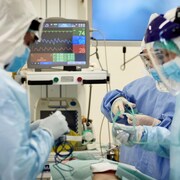 Des médecins et des infirmières qui portent des blouses chirurgicales, des lunettes et des masques se préparent à pratiquer une intervention chirurgicale.