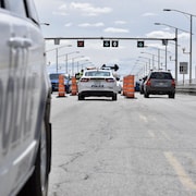 Des policiers parlent à des automobilistes sur le pont, entourés de cônes orange.