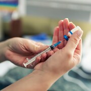 Gros plan sur les mains d'une personne manipulant une seringue et une fiole de vaccin contre la COVID-19. 