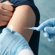 Une main tenant une seringue s'approche d'un bras pour administrer un vaccin. 