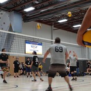 Des joueurs de volleyball échangent des ballons dans un gymnase.