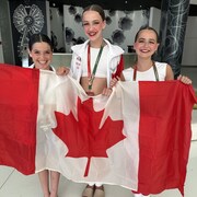 Trois adolescentes posent avec un drapeau canadien.