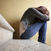 Une adolescente dans un escalier, elle a la tête dans ses propres bras.