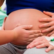 Plusieurs mains entourent le ventre d'une femme enceinte.