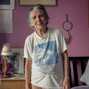 Une vieille femme debout dans sa chambre.
