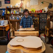 Un homme portant une chemise à carreaux, debout dans un atelier de fabrication de guitares.