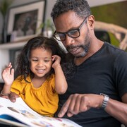 Une fillette et son père en train de livre un livre.