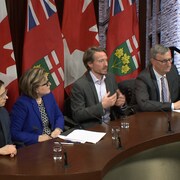 Quatre officiels du ministère de la Santé de l'Ontario, dont les docteurs David Williams, médecin hygiéniste en chef, et Barbara Yaffe, assistante au médecin hygiéniste en chef, font une déclaration, assis derrière un bureau. Les drapeaux canadien et ontarien sont à l'arrière-plan.