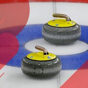 Deux pierres de curling sont sur la surface glacée du jeu dans le cercle bleu.