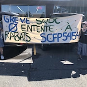 Des manifestants avec une affiche qui indique "Grève SQDC, pas d'entente à rabais SCFP5454". 