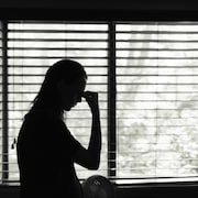 L'ombre d'une femme qui se tient la tête devant une fenêtre, le tout en noir et blanc.