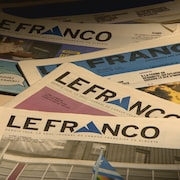 Des journaux Le Franco sont étalés sur une table. 