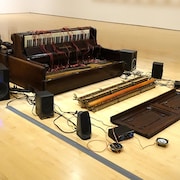 Un piano déconstruit et des haut-parleurs sur le sol d'une salle d'exposition.