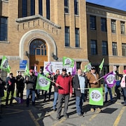 Des manifestants devant un bâtiment avec des affiches de la C S N.