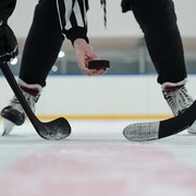 Un arbitre tenant une rondelle de hockey au-dessus d'une patinoire avec deux joueurs qui tendent leurs bâtons.