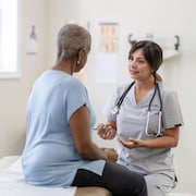 Une infirmière discute avec une patiente assise sur une table d'examen.