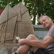 James W. Cook devant un bateau sculpté dans le sable.