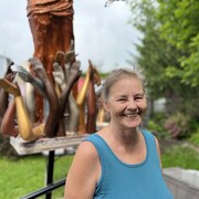 Une femme souriante devant une sculpture.