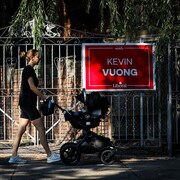 Une femme avec une poussette marche devant une affiche de campagne électorale.