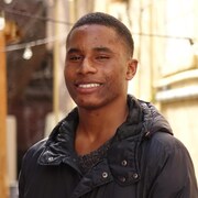Un homme souriant dans une ruelle avec des lumières suspendues.