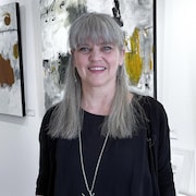Une femme souriante qui pose devant des oeuvres exposées sur les murs d'une galerie.