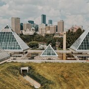 Les pyramides de verre du jardin botanique avec en toile de fond le centre ville d'Edmonton par une journée partiellement ennuagée de juin. Photo prise le 16 juin 2022.