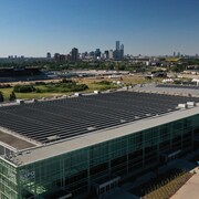 Plan aérien de panneaux solaires noirs montés sur une structure métallique argentée sur un toit en béton gris avec en arrière plan le centre-ville d'Edmonton par une journée ensoleillée d'été. 18 août 2022.
