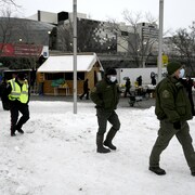 Deux agents de conservation accompagnés d'un policier marchent dans la neige dans une manifestation.