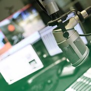 Un micro dans un studio de radio avec des écrans et une console en arrière-plan. 