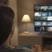 Une femme assise dans un salon qui regarde une télévision où l'on peut voir une sélection de contenus dans une plateforme de diffusion en continu.