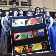 Un groupe de jeunes étudiants qui tiennent une grande courtepointe lors de leur cérémonie de remise de diplômes.