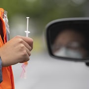 Une personne tient une seringue près d'un conducteur qui s'apprête à recevoir un vaccin.