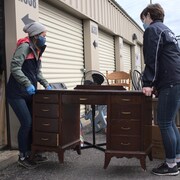 Deux bénévoles de Shelter Movers transportent un meuble qui appartient à une femme victime de violence conjugale ayant quitté sa demeure.