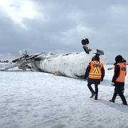 Deux enquêteurs du BST devant l'avion renversé.