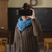 Une femme qui porte un casque de réalité virtuelle debout dans une salle de classe.